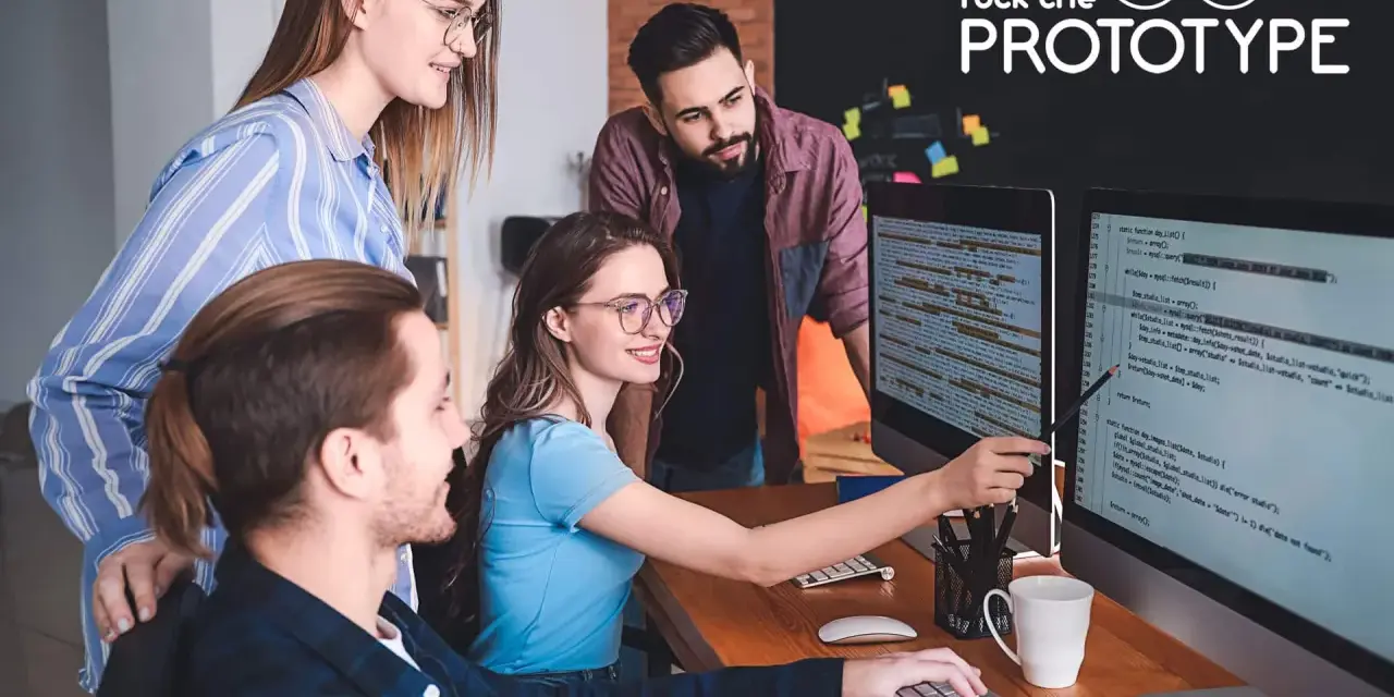 Ein Team von vier Personen arbeitet im **mob programming** an einem Projekt. Sie blicken auf zwei Bildschirme mit Code.