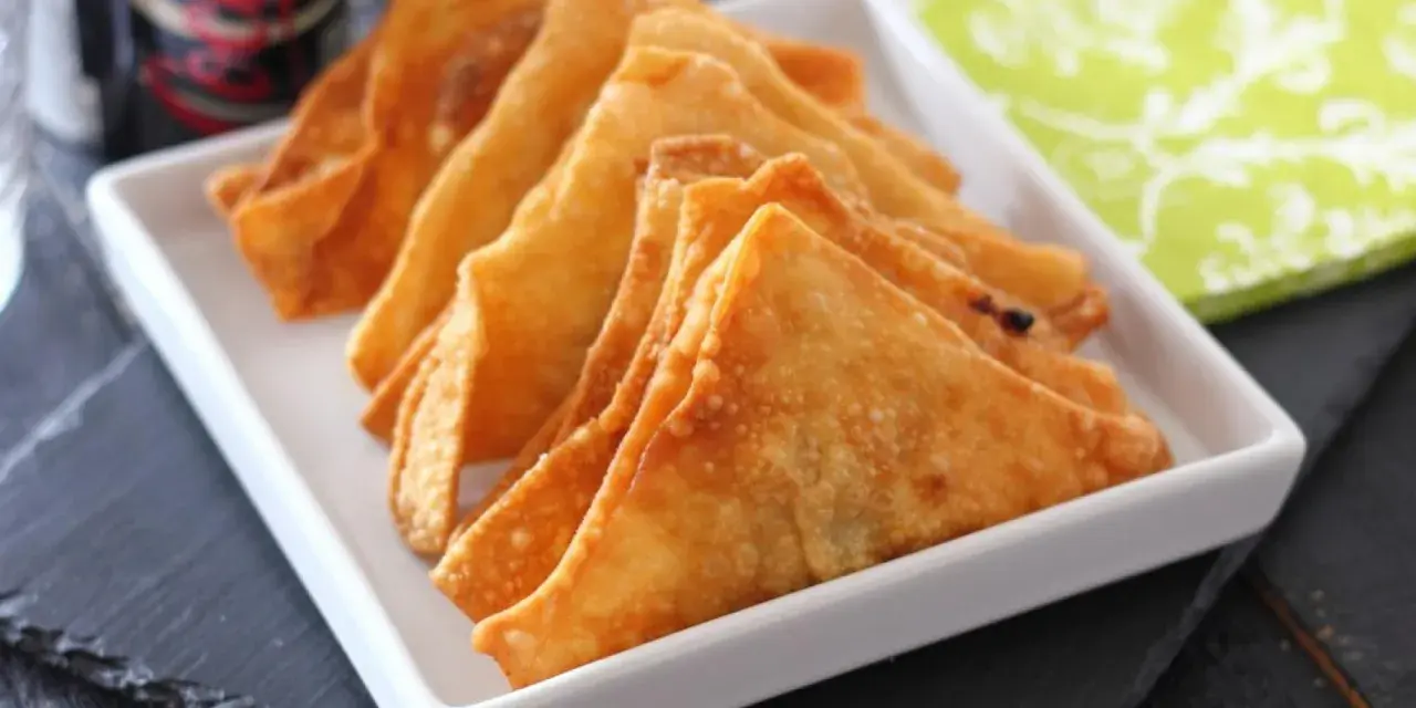 Wontons fritos dorados y crujientes en un plato blanco.