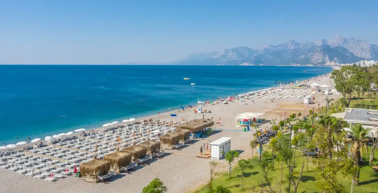 Piękna plaża z rzędami leżaków i parasoli, gdzie jest Antalya. Błękitne morze i góry w tle tworzą idealny krajobraz.