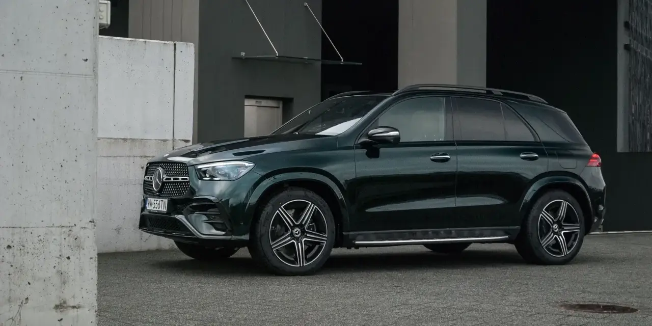 Elegancki, ciemnozielony Mercedes GLE 2025 zaparkowany przed nowoczesnym budynkiem.