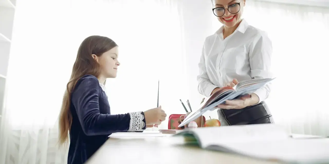 Nauczycielka pomaga dziecku z dysleksją w szkole, cierpliwie tłumacząc materiał z książki.