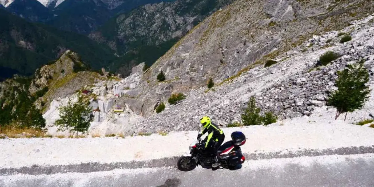 Motociclista in abbigliamento giallo fluo affronta il passo del vestito, tra cave di marmo e montagne imponenti.