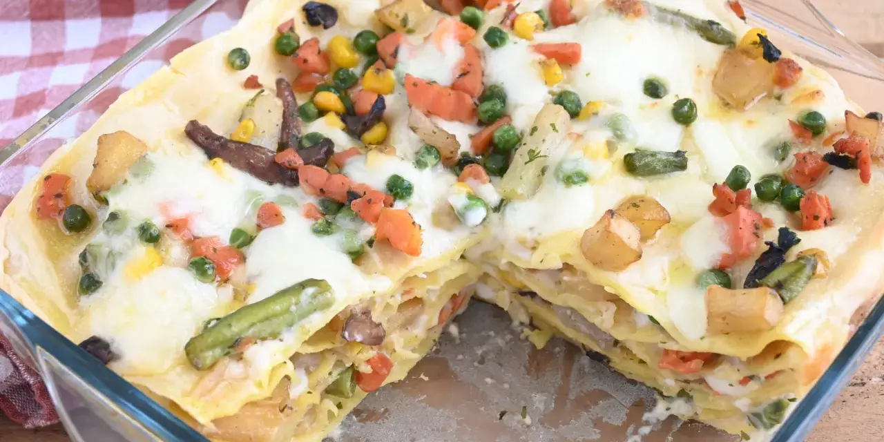 Lasagne di verdure dorate e filanti, con piselli, carote, patate e fagiolini, in una teglia di vetro.