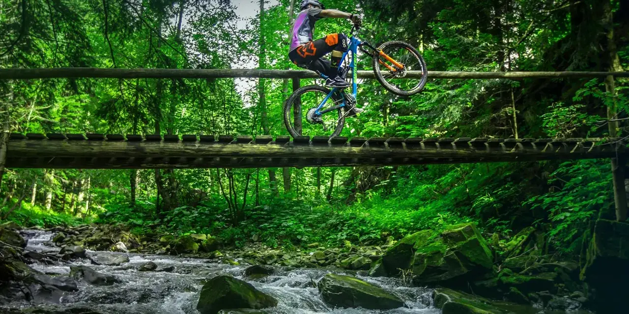 Rowerzysta na drewnianym moście nad potokiem, odkrywa nowe trasy rowerowe Zakopane.