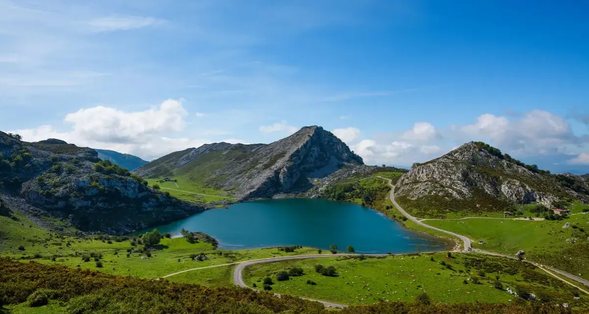 Lago azul rodeado de montañas verdes y caminos sinuosos, parte de la red de parques nacionales.
