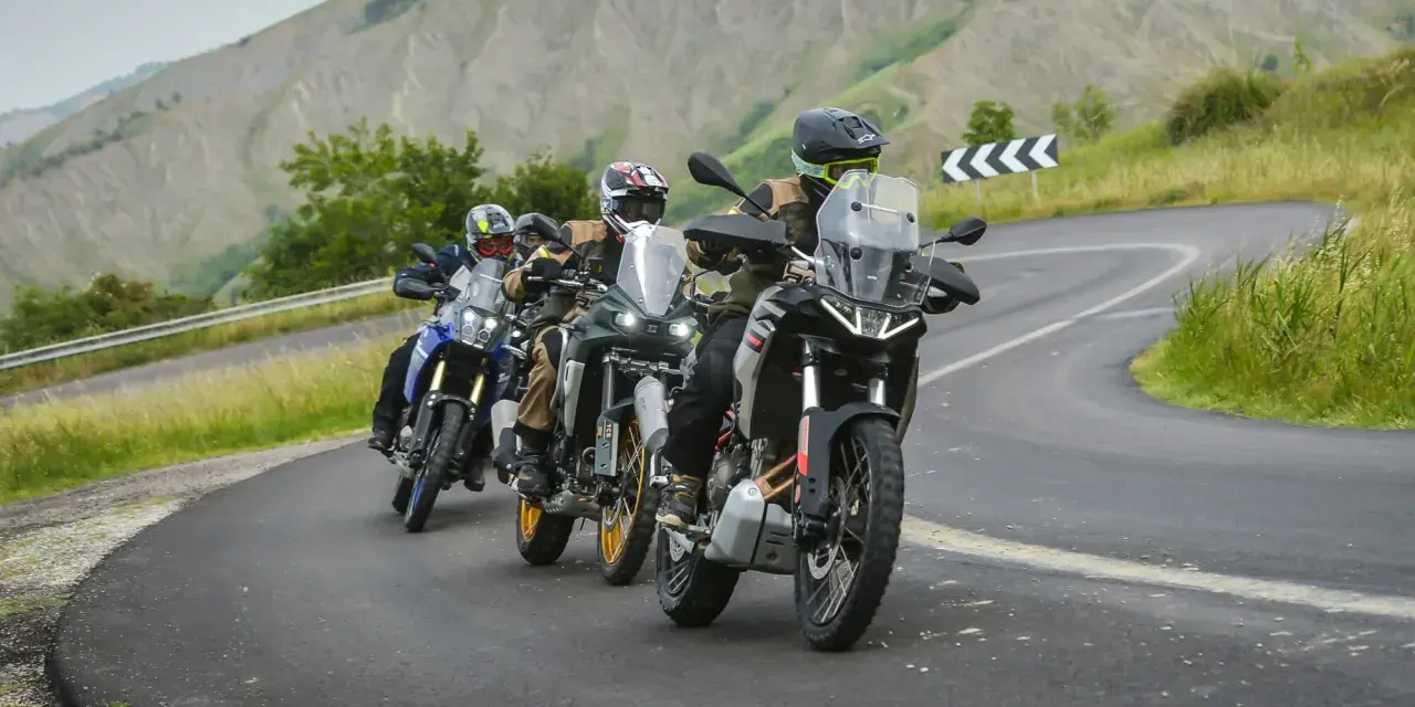 Quattro motociclisti in fila su una strada tortuosa tra colline verdi. Sei motociclista se ami l'avventura.