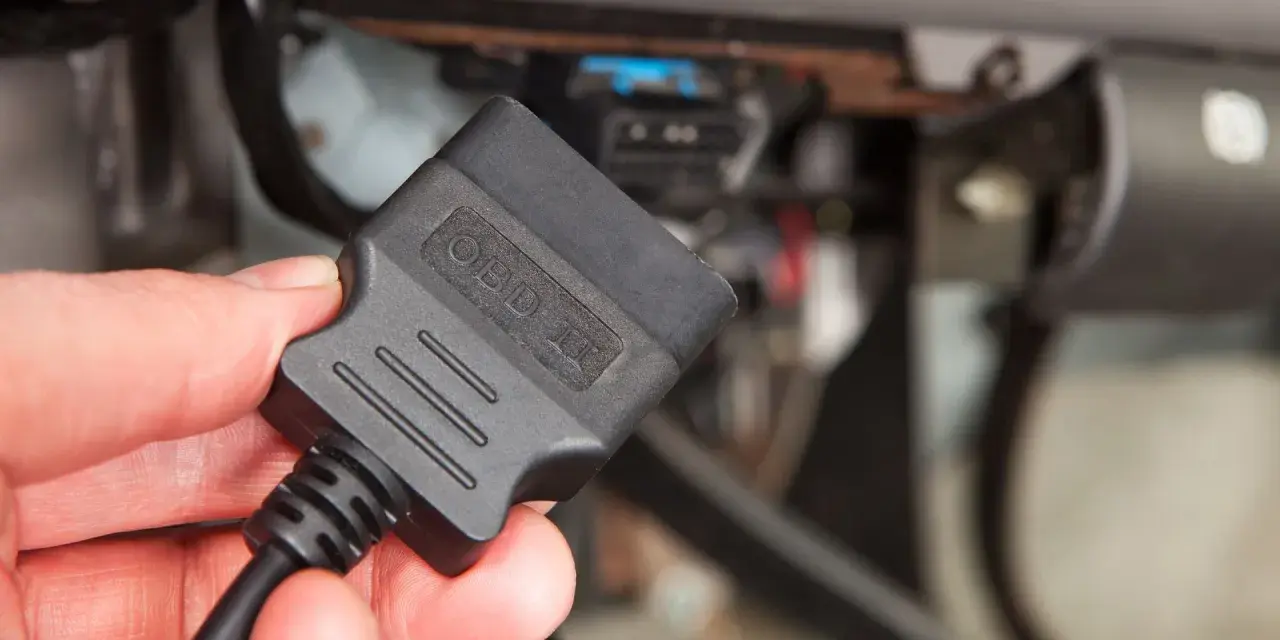 Dłoń trzyma adapter OBD II, gotowy do podłączenia i sprawdzenia kodu błędu w samochodzie.