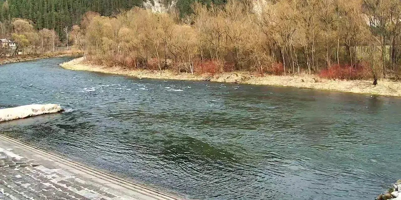 Szeroka rzeka płynie wśród drzew i skalistych zboczy.