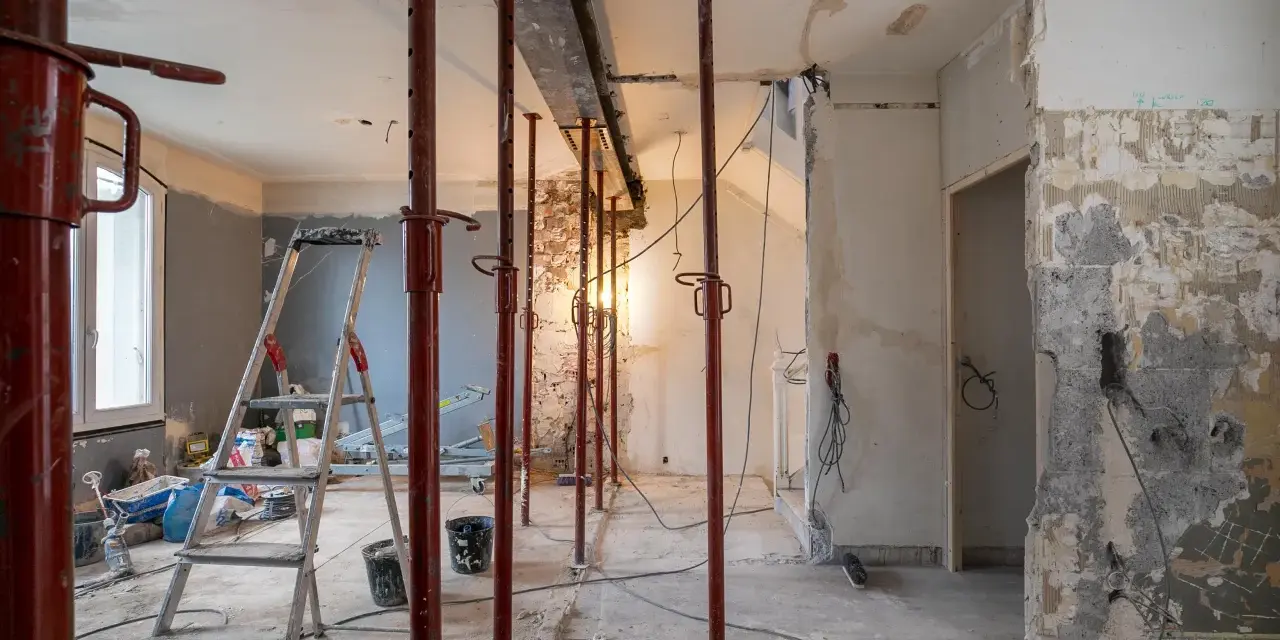 Chantier en cours : étais rouges soutenant un linteau, murs abattus, échelle et matériaux. Préparation pour une ouverture mur porteur.