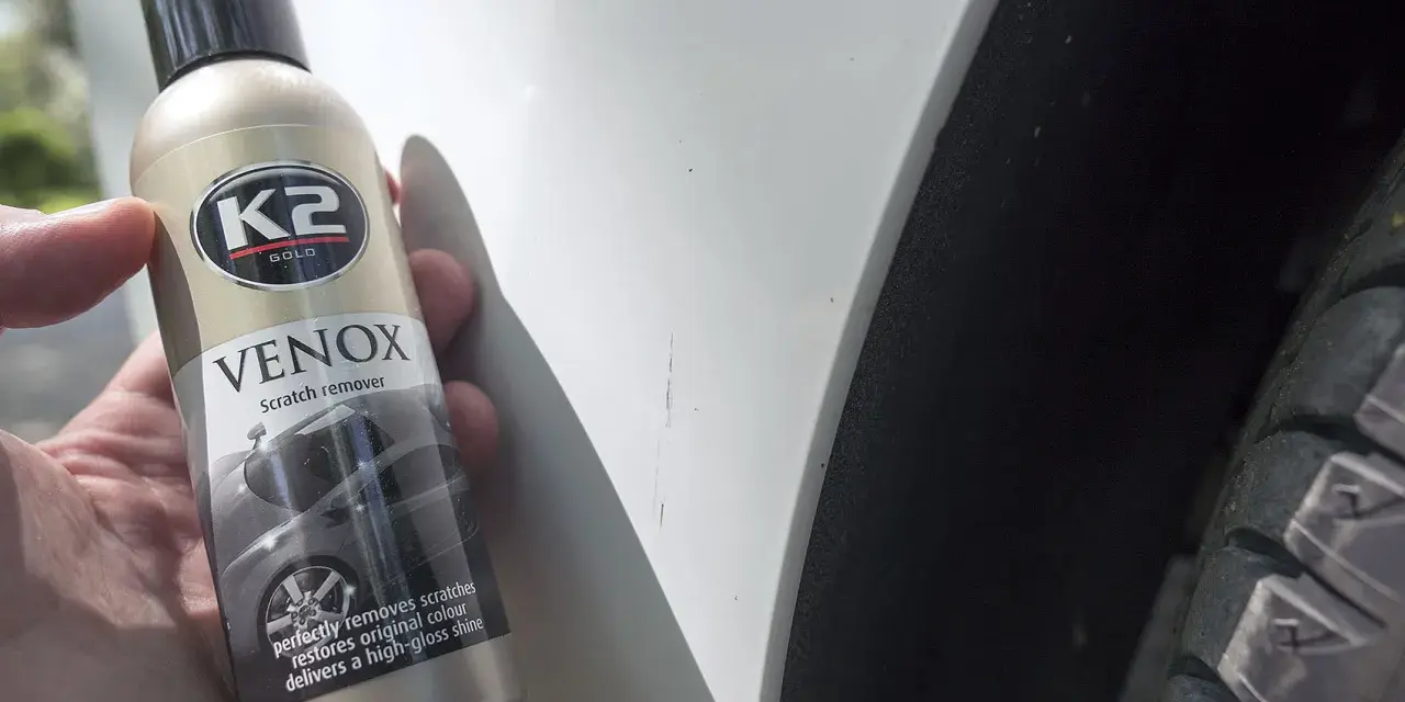 Jak usunąć głębokie rysy na lakierze? Butelka K2 VENOX Scratch remover obok białego lakieru z widocznymi zarysowaniami.