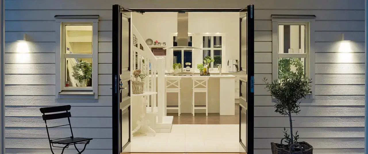 Välkomnande entré inspiration utomhus. Öppna dörrar leder in till ett ljust kök med köksö och trappa.