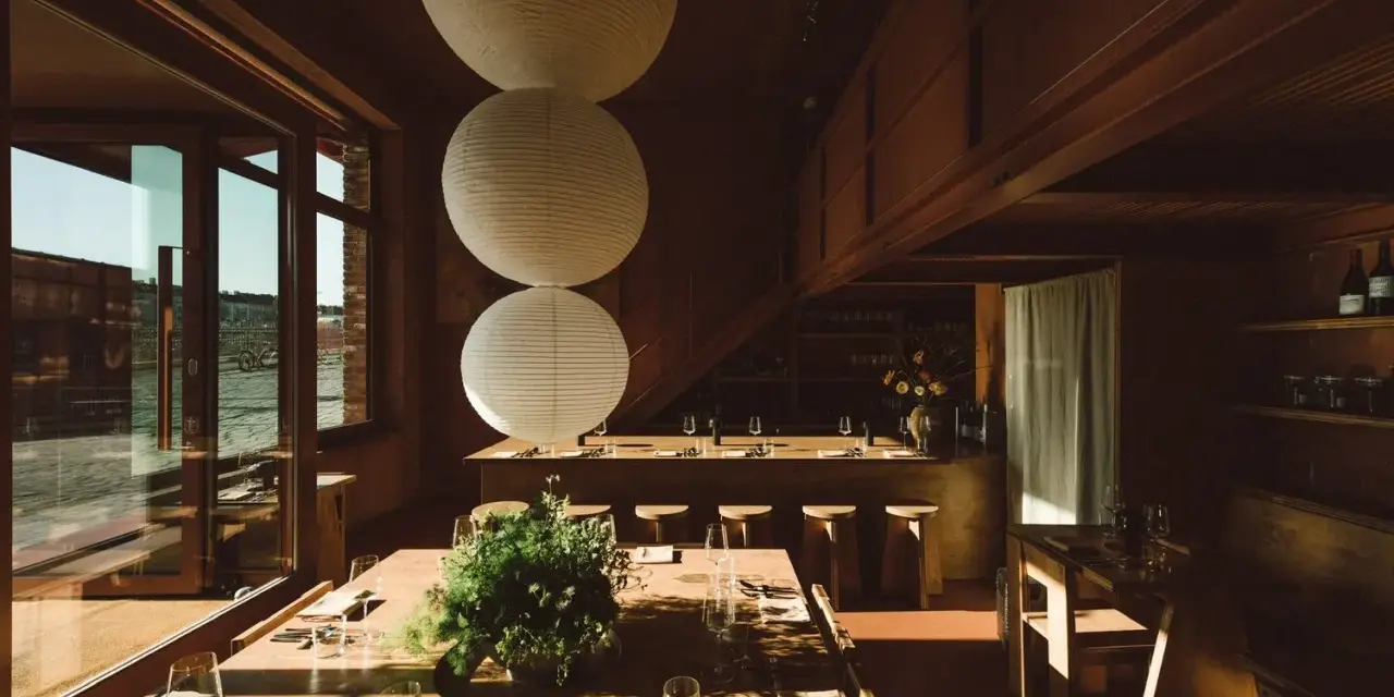Gemütliches Restaurant in **Aerde Berlin** mit Holztischen, großen Papierlampen und Blick auf das Wasser.