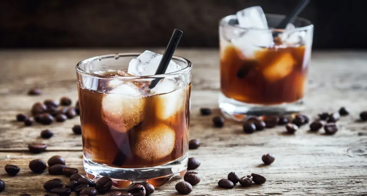 Dwa szklanki z lodem i ciemnym napojem, otoczone ziarnami kawy. Idealny czarny rusek drink na drewnianym blacie.