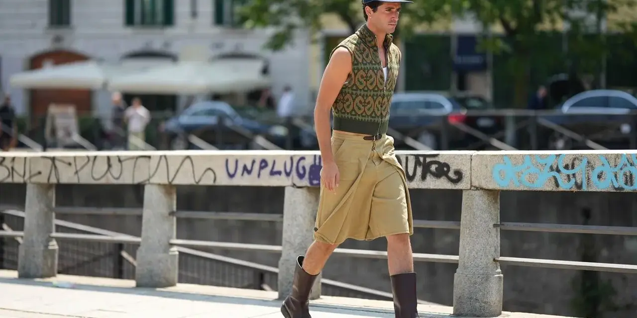 Uomo con un elegante outfit sportivo estivo: gilet a fantasia, bermuda color sabbia e stivali.