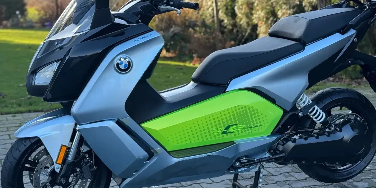 Srebrno-czarny skuter elektryczny BMW C Evolution z zielonym akcentem i napisem "C Evolution" na boku, stojący na chodniku.