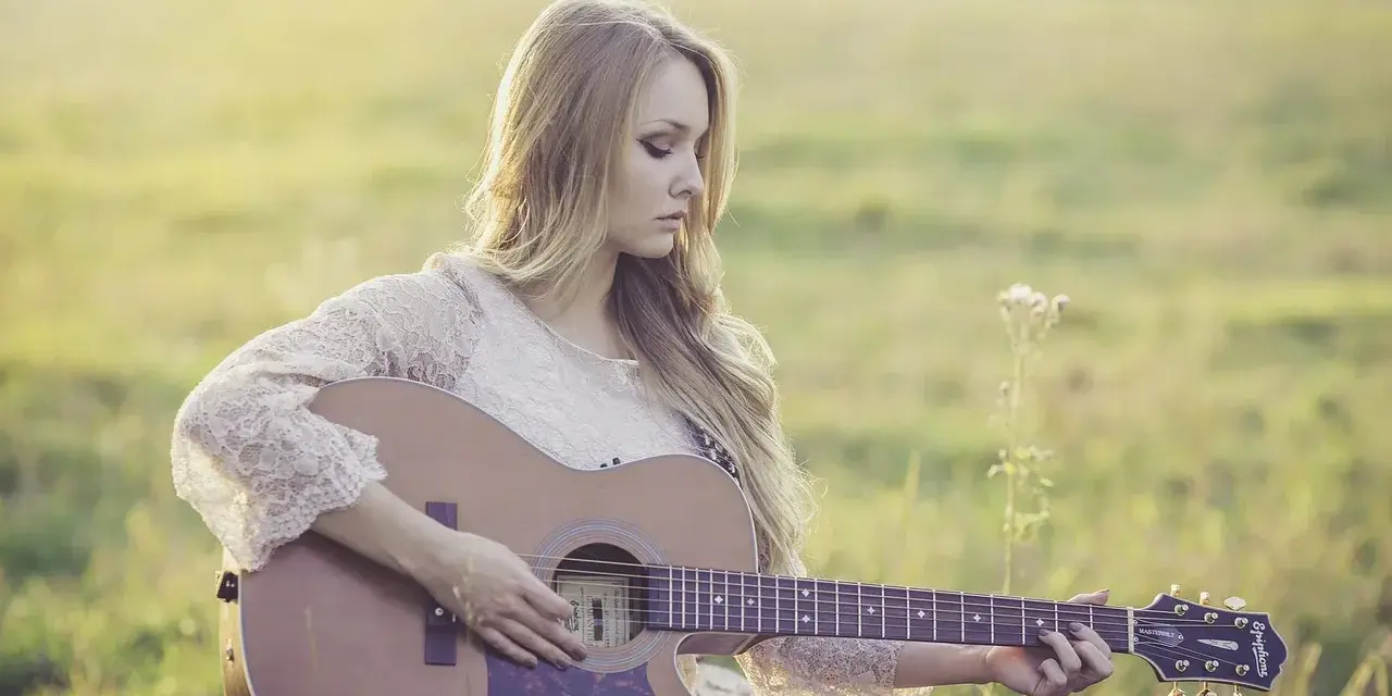 Blondynka w koronkowej sukience gra na gitarze w słonecznym polu. To jak remaster starych wspomnień, pełen ciepła i nostalgii.