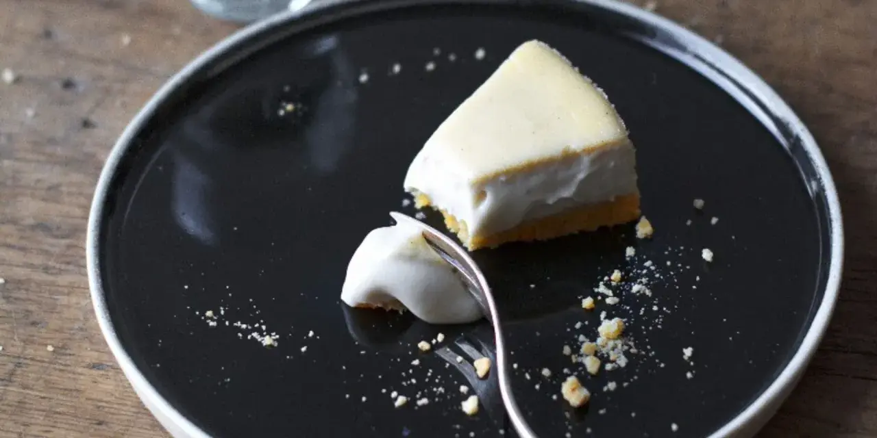 Un trozo de tarta de queso cremoso, con una porción ya probada, sobre un plato negro.