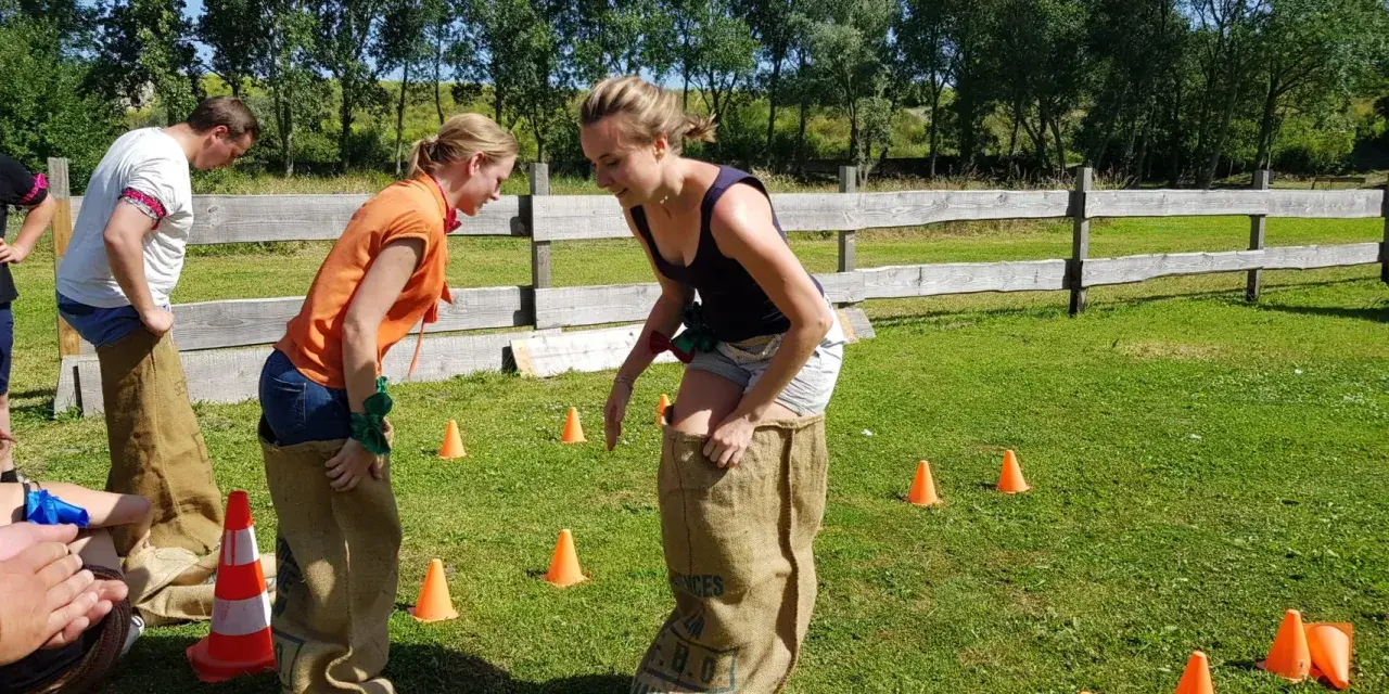 Des collègues s'amusent lors de jeux entre collègues de travail, sautant dans des sacs en toile de jute sur une pelouse verte.