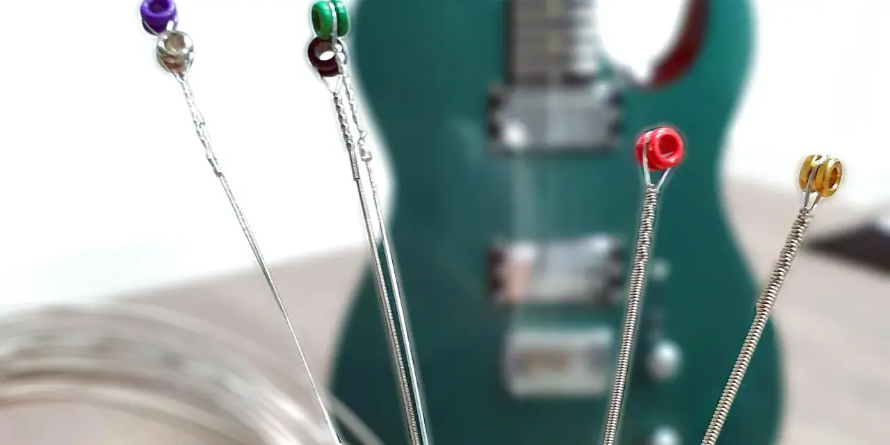 Vier Gitarrensaiten mit farbigen Enden (lila, grün, rot, gold) liegen vor einer grünen E-Gitarre. Die besten E-Gitarren-Saiten für deinen Sound.