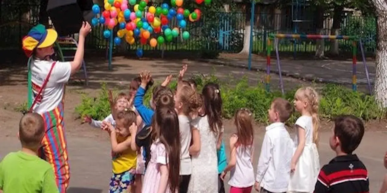 Klaun wypuszcza balony dla dzieci. Czy są zerówki w szkołach? Dzieci cieszą się zabawą na świeżym powietrzu.