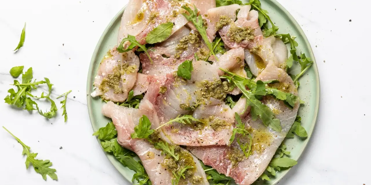 Deliziosi antipasti di pesce crudo, affettati sottili e conditi con erbe aromatiche e olio, serviti su un letto di rucola fresca.