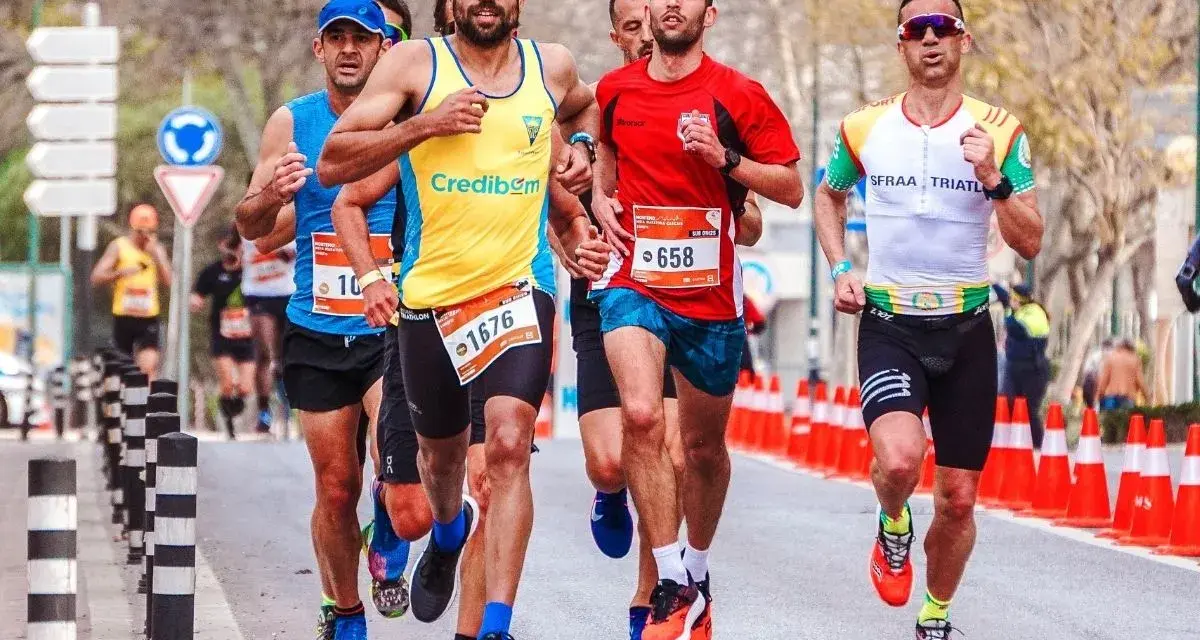 Atleti in gara, con pettorali visibili, corrono su strada. Le tabelle ripetute corsa principianti sono un ottimo modo per iniziare.