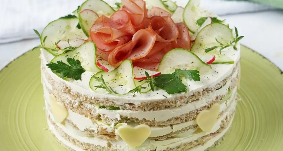 Herzhafter Kuchen mit Schichten aus Brot, Frischkäse, Gurken und Schinken. Dekoriert mit Radieschen, Kräutern und Käseherzen.