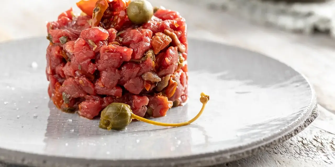 Deliziosa tartare di manzo, guarnita con capperi e pomodori secchi, servita su un piatto grigio.