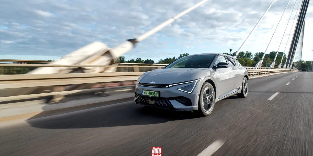Szary Kia EV6 jedzie po moście w słoneczny dzień.