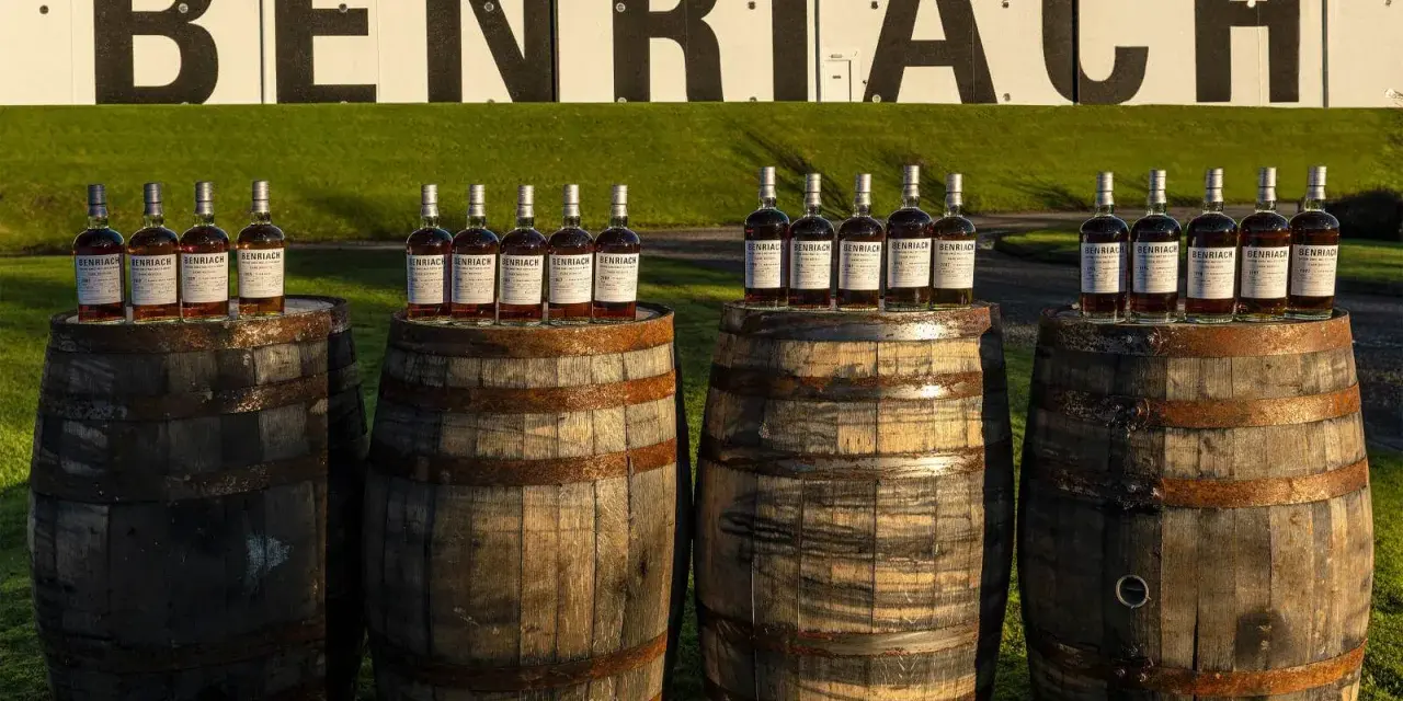Butelki whisky Benriach stoją na beczkach, które czekają na dojrzewanie w pomieszczeniu.