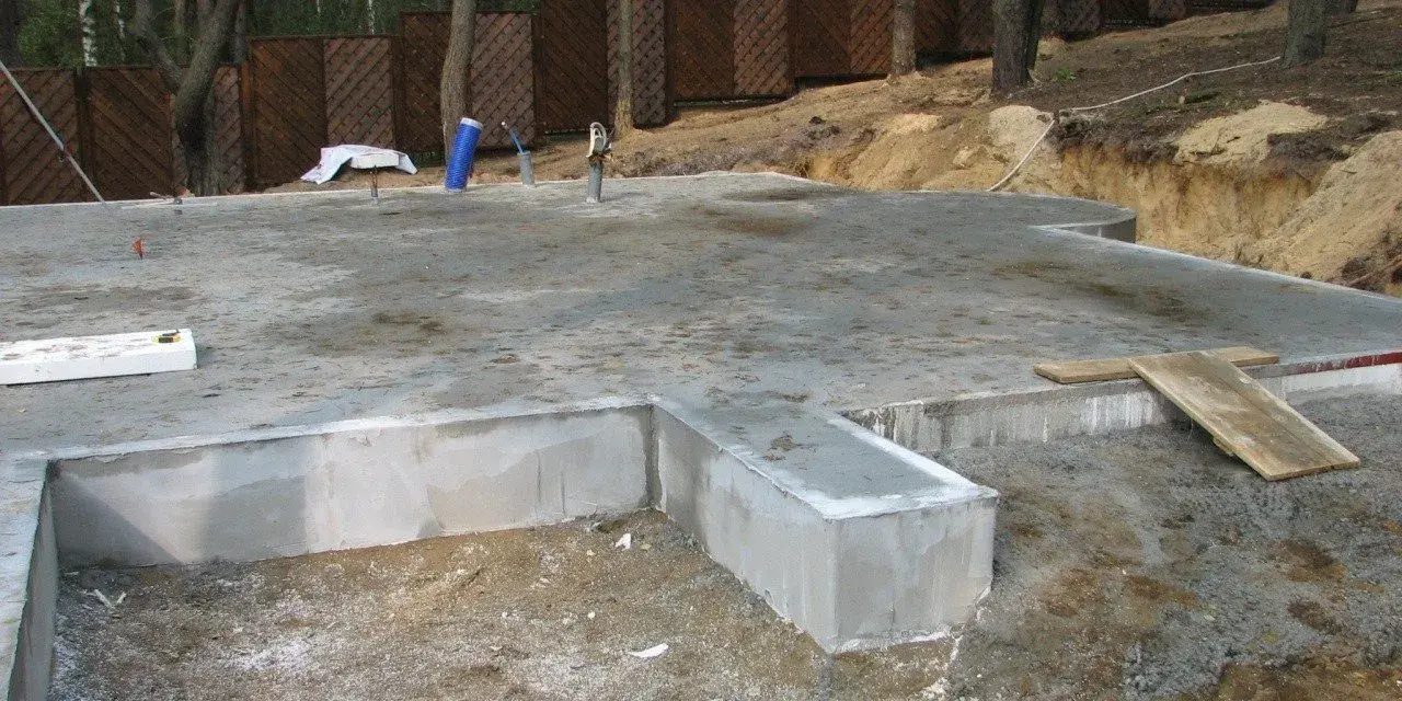Fundament płytowy w trakcie budowy, z widocznymi elementami betonowymi i zbrojeniem.