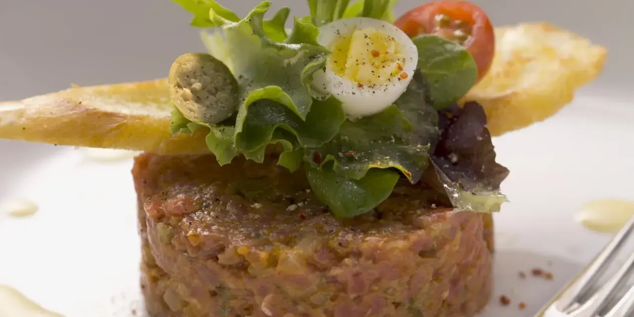 Un délicieux tartare de bœuf, garni d'une salade fraîche, d'un œuf de caille et de croûtons. Une recette parfaite pour un repas raffiné.