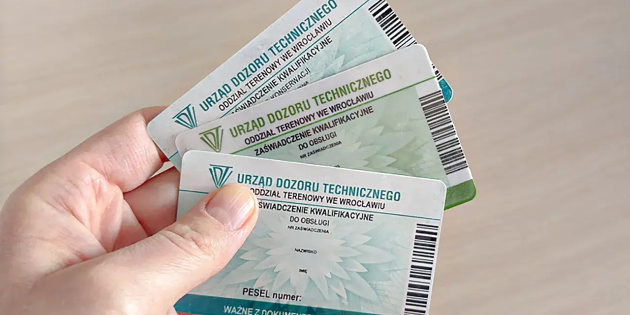 Dłoń trzyma kilka zaświadczeń kwalifikacyjnych Urzędu Dozoru Technicznego, potwierdzających uprawnienia HDS.