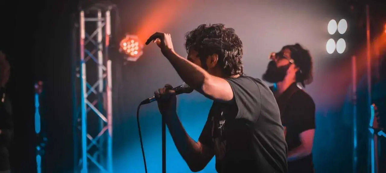 Ein Sänger mit Mikrofon auf einer Bühne, umgeben von Bühnenlichtern. Das ist, was Indie-Musik ausmacht: Leidenschaft und Energie.