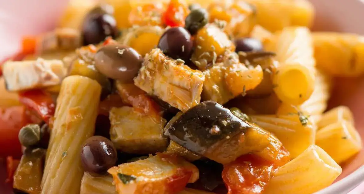 Un piatto invitante di pasta con pesce, arricchito da olive nere, capperi e verdure colorate.