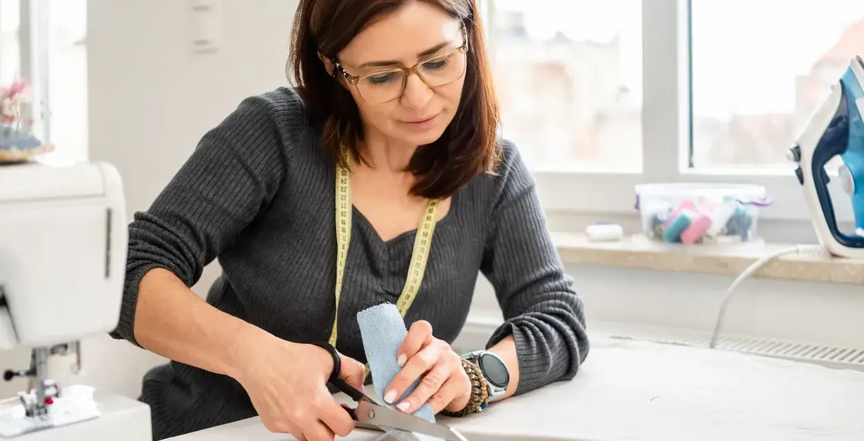 Une couturière utilise des ciseaux pour couper du tissu, montrant l'importance des différents types de ciseaux de couture pour un travail précis.