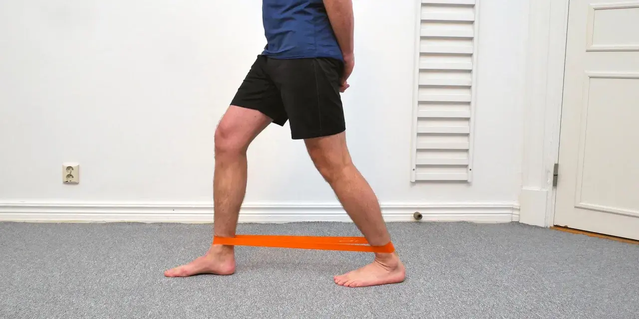 Man tränar för att stärka stela fotleder med ett orange träningsband runt anklarna.