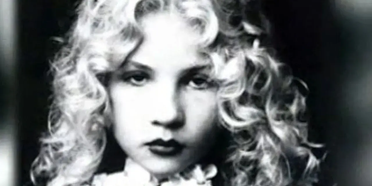 Portrait en noir et blanc d'Eva Ionesco enfant, aux boucles blondes et au regard intense.