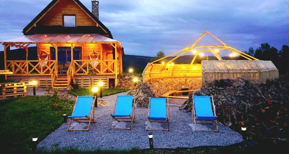 Drewniany domek z werandą, jacuzzi pod zadaszeniem i leżakami w malowniczej okolicy.