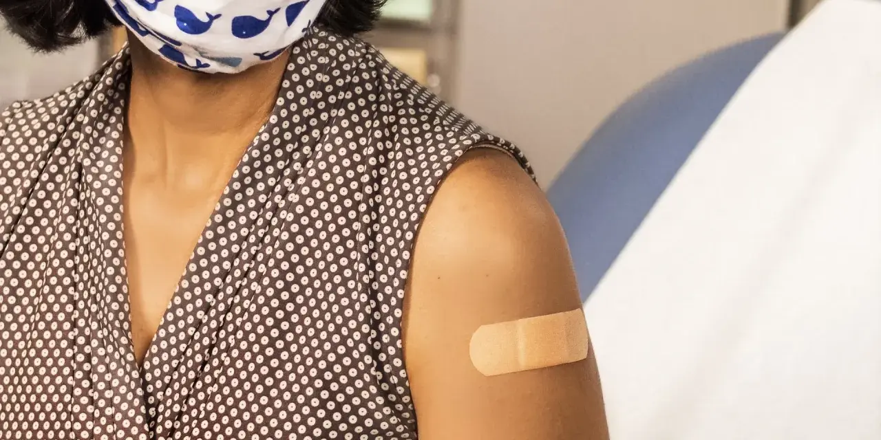 Osoba w maseczce z wielorybami ma plaster na ramieniu po szczepieniu. Dbanie o zdrowie, w tym szczepionka HPV, to ważny krok.