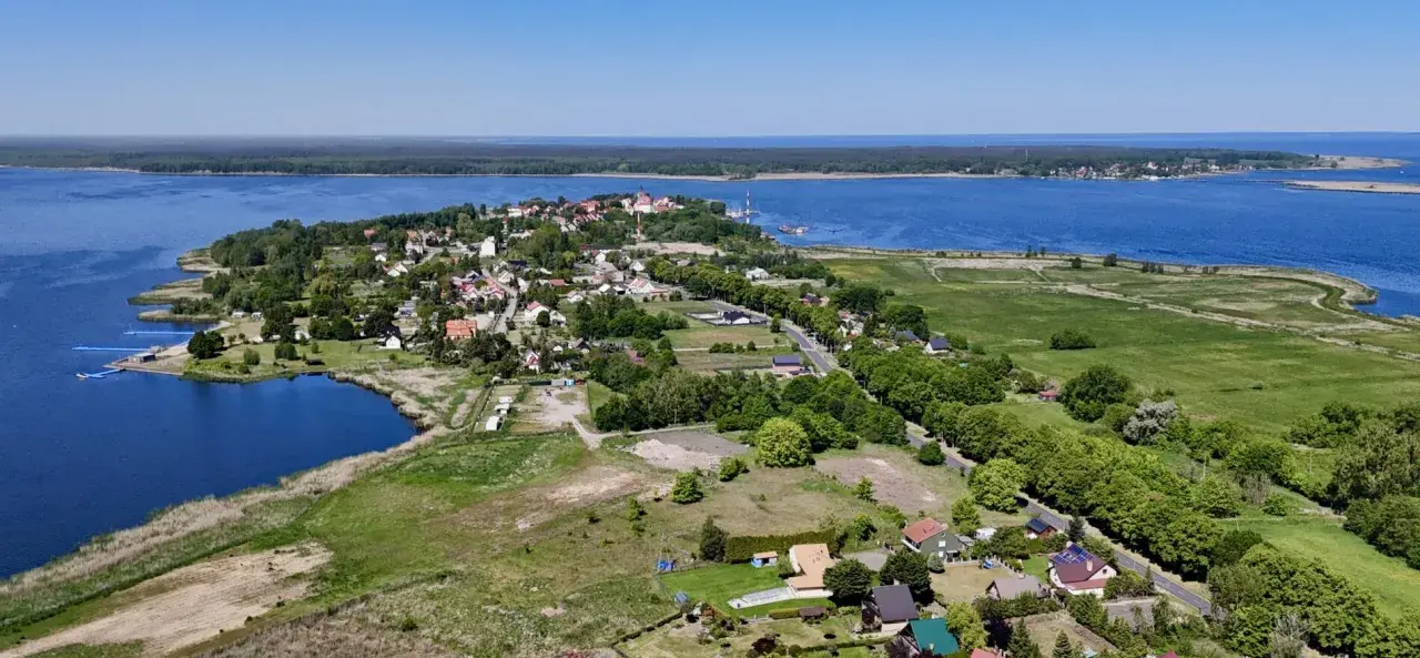 Widok na Nowe Warpno z lotu ptaka. Widać jezioro, zabudowania, las i zielone pola. Idealne miejsce na wypoczynek nad wodą.