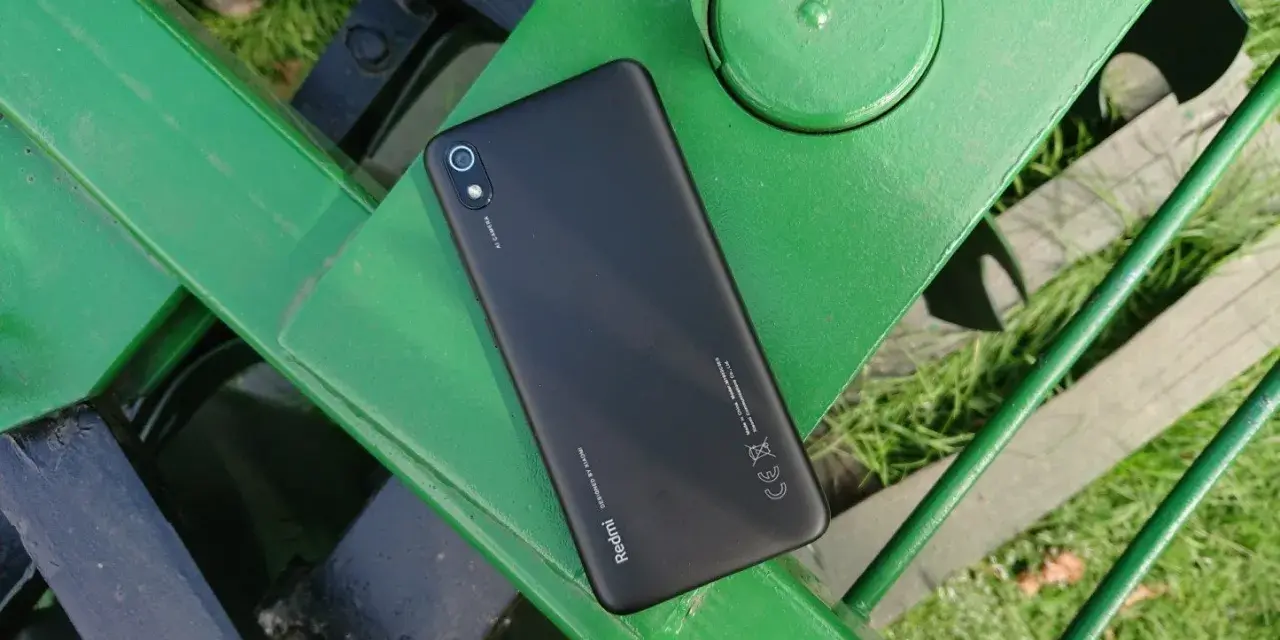 Czarny telefon Xiaomi Redmi 7 leży na zielonej, metalowej ławce.