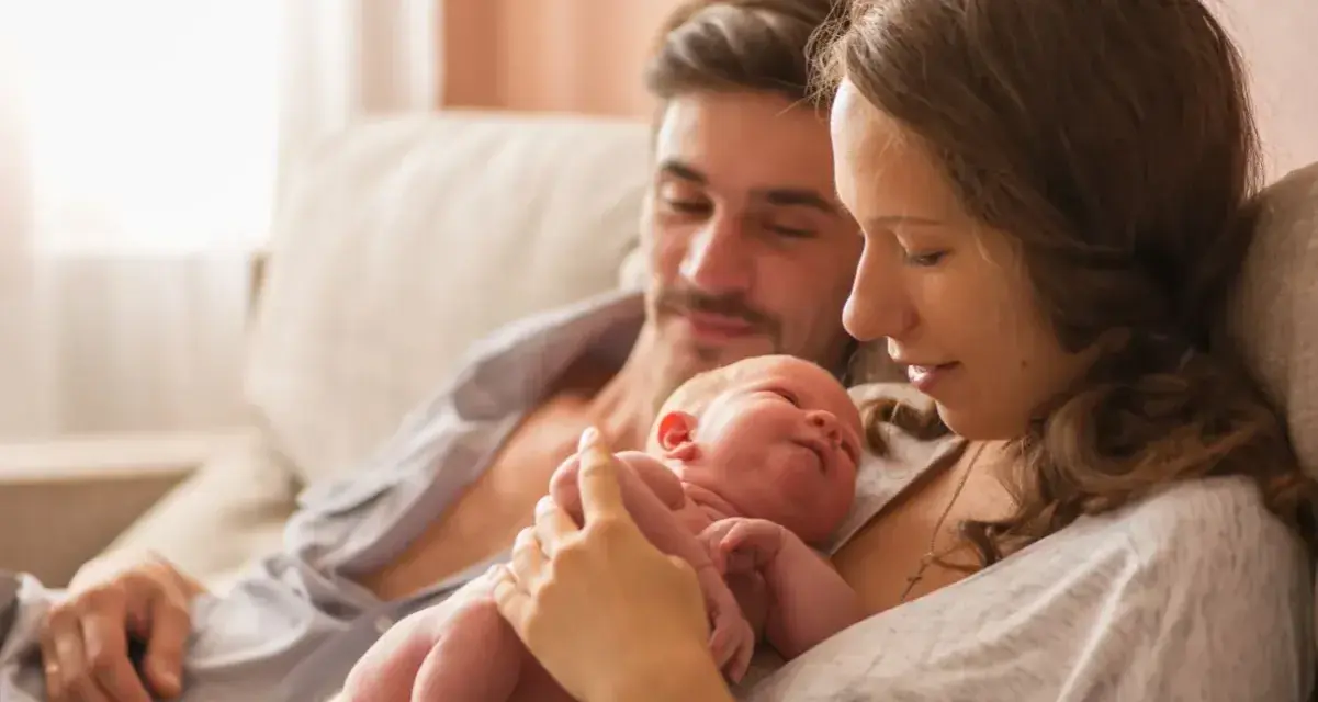 Mama tuli noworodka, tata patrzy z miłością. To piękny obraz opieki na żone po porodzie, pełen czułości i wsparcia.
