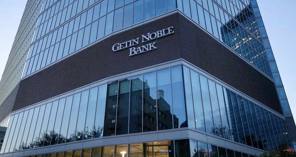 Nowoczesny budynek banku z napisem "GETIN NOBLE BANK". W szklanej fasadzie odbijają się inne budynki i drzewa.