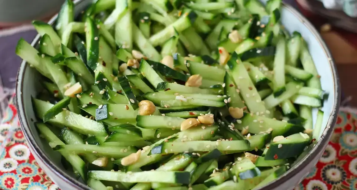Una ciotola di fresca insalata di cetrioli tagliati a julienne, condita con semi di sesamo e arachidi croccanti.