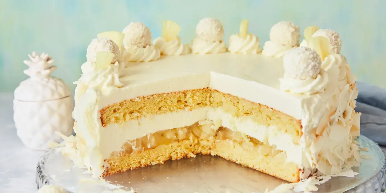 Eine köstliche Piña Colada Torte mit Kokosraspeln und Ananasstücken, verziert mit Sahnetuffs und Pralinen.