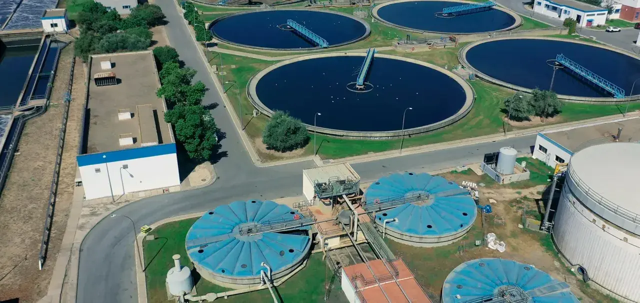Vista aérea de una planta de depuración de aguas con grandes tanques circulares y estructuras industriales.