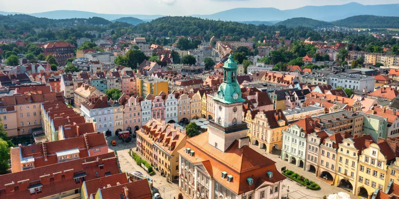 Widok z lotu ptaka na kolorowy rynek starego miasta z wieżą ratuszową i górzystym tłem.