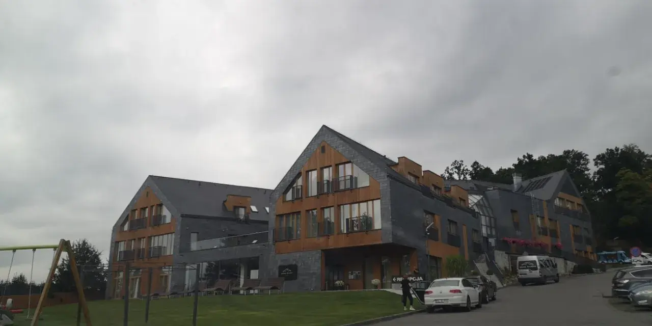 Nowoczesny hotel z drewnianymi elementami i kamienną elewacją. Na trawniku plac zabaw. Wiele pozytywnych osada-sniezka opinie potwierdza jego urok.