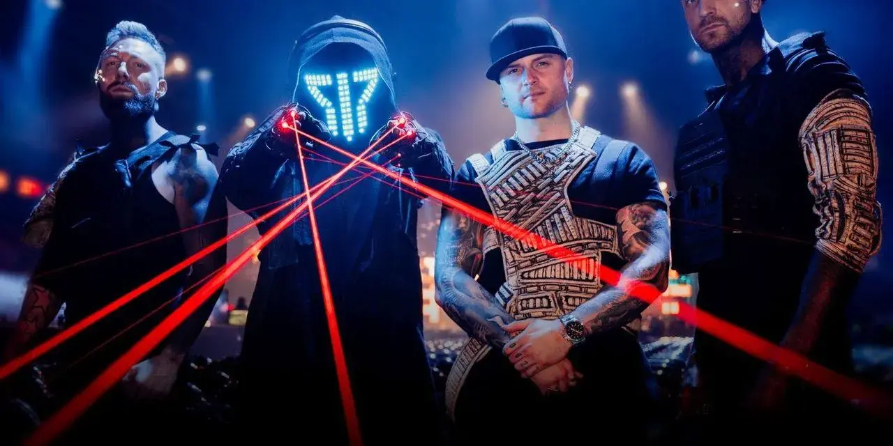 Czterech mężczyzn w futurystycznych strojach, z maską LED i czerwonymi laserami na scenie.